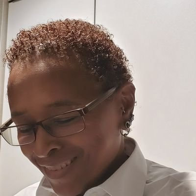 Lynnell Stephani Long, a Black intersex woman, smiling and looking down from the camera. She has glasses and short hair.